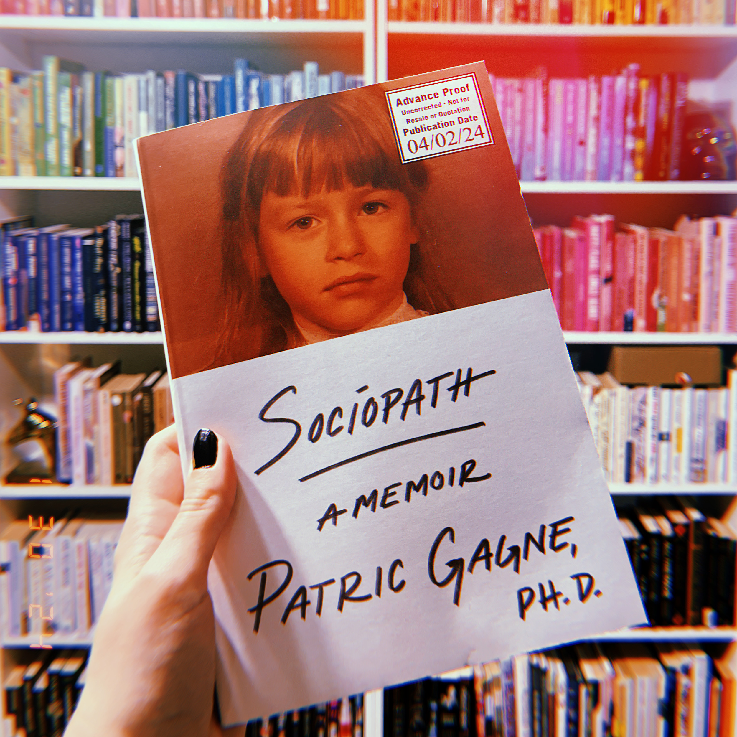 A hand holding up an advanced reader copy of Sociopath: A Memoir by Patric Gagne. Behind is a colorful bookshelf.
